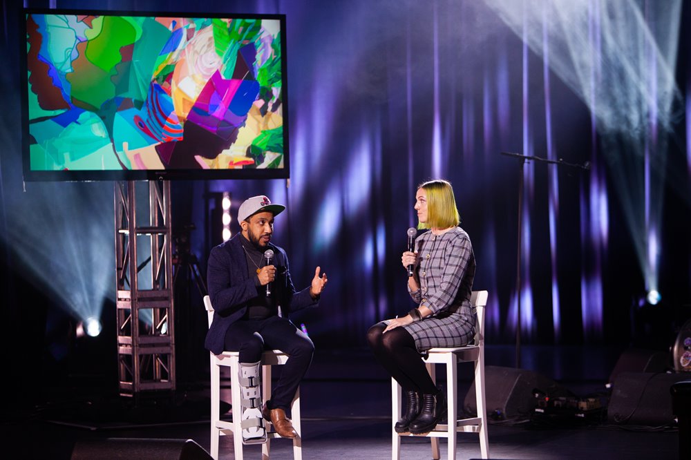 Luke Reece & Jennifer Alicia sit on chairs on stage