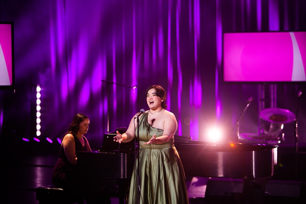 Midori Marsh dresses in a green dress stretches her arms out while singing into a microphone