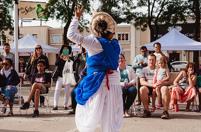 A woman dances in front of a seated crowd on a street.