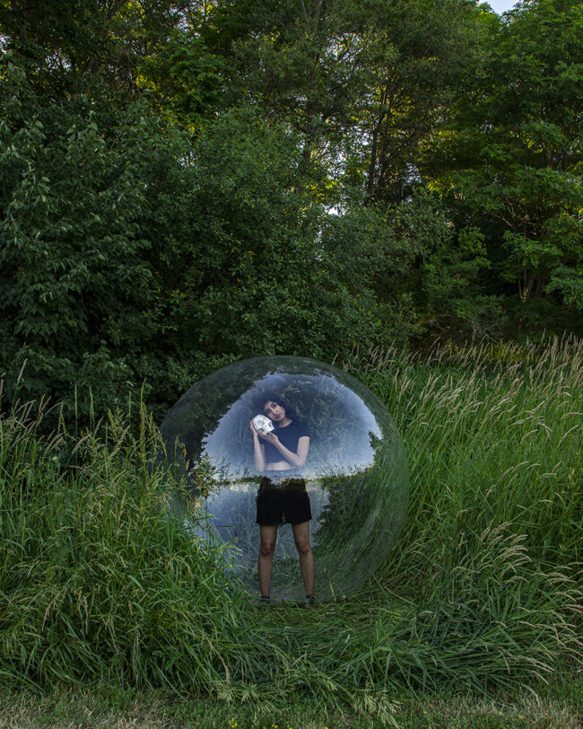 A photo of a person inside a large orb in a green field.