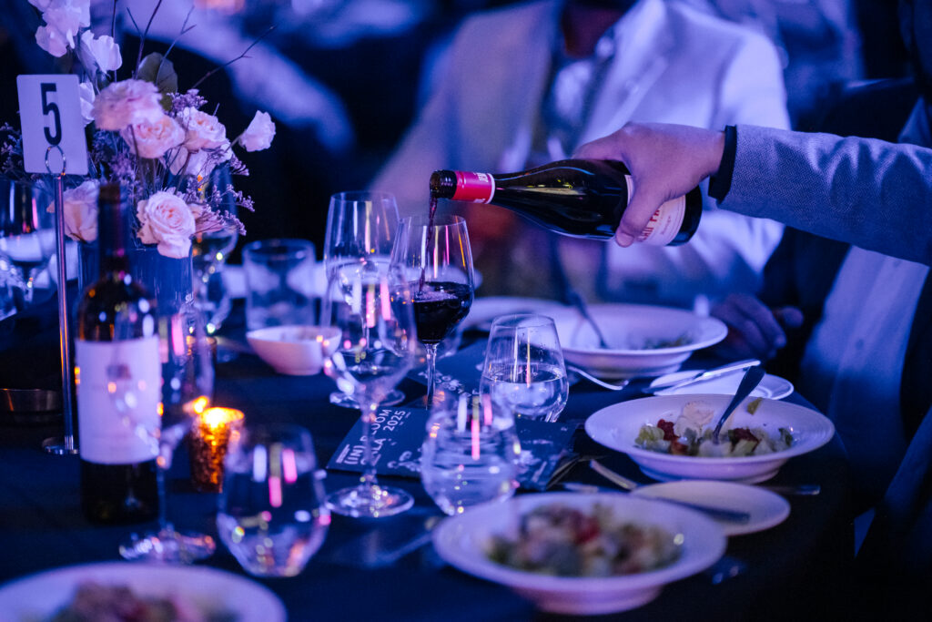 Someone pours red wine into a wine glass at an elegant dinner table with flowers.