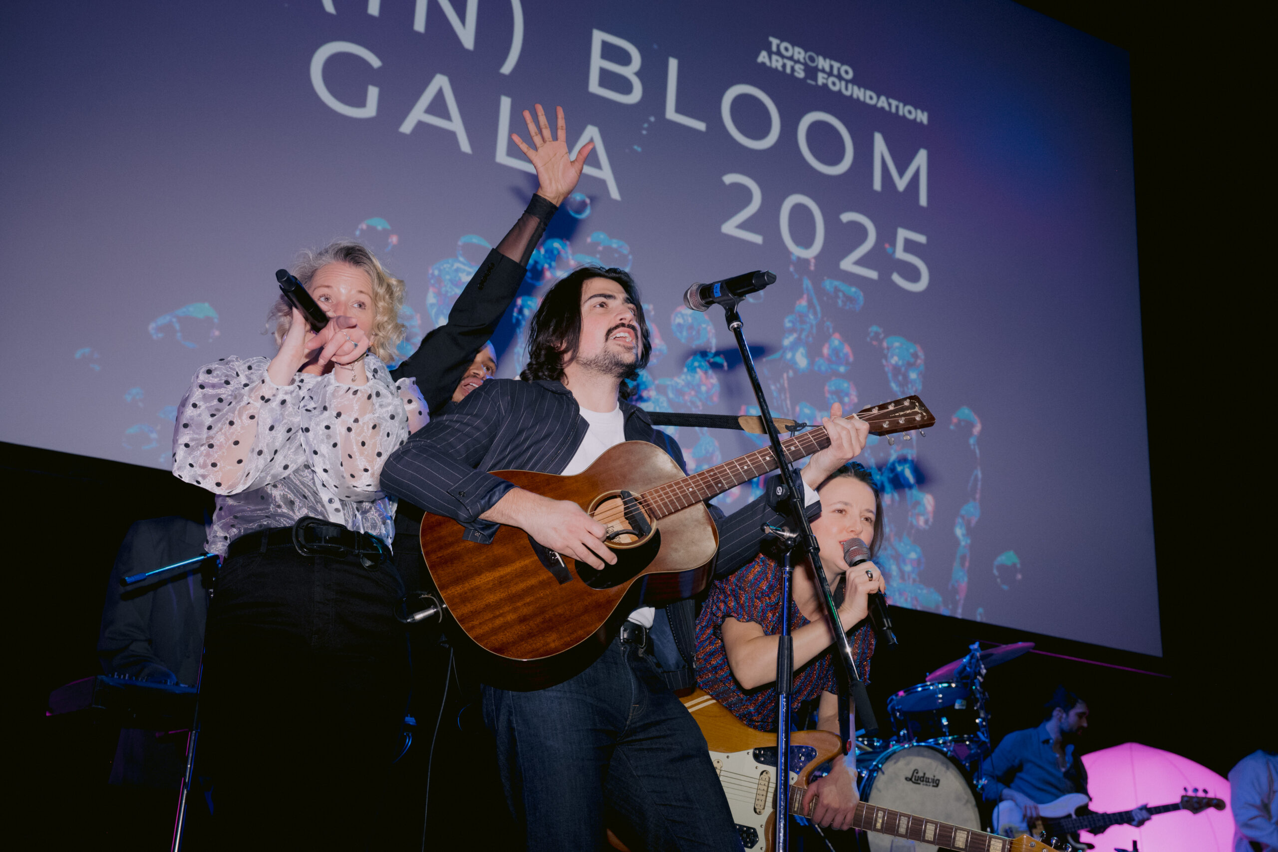 A band plays on stage in front of a sign that reads (In) Bloom Gala 2025.