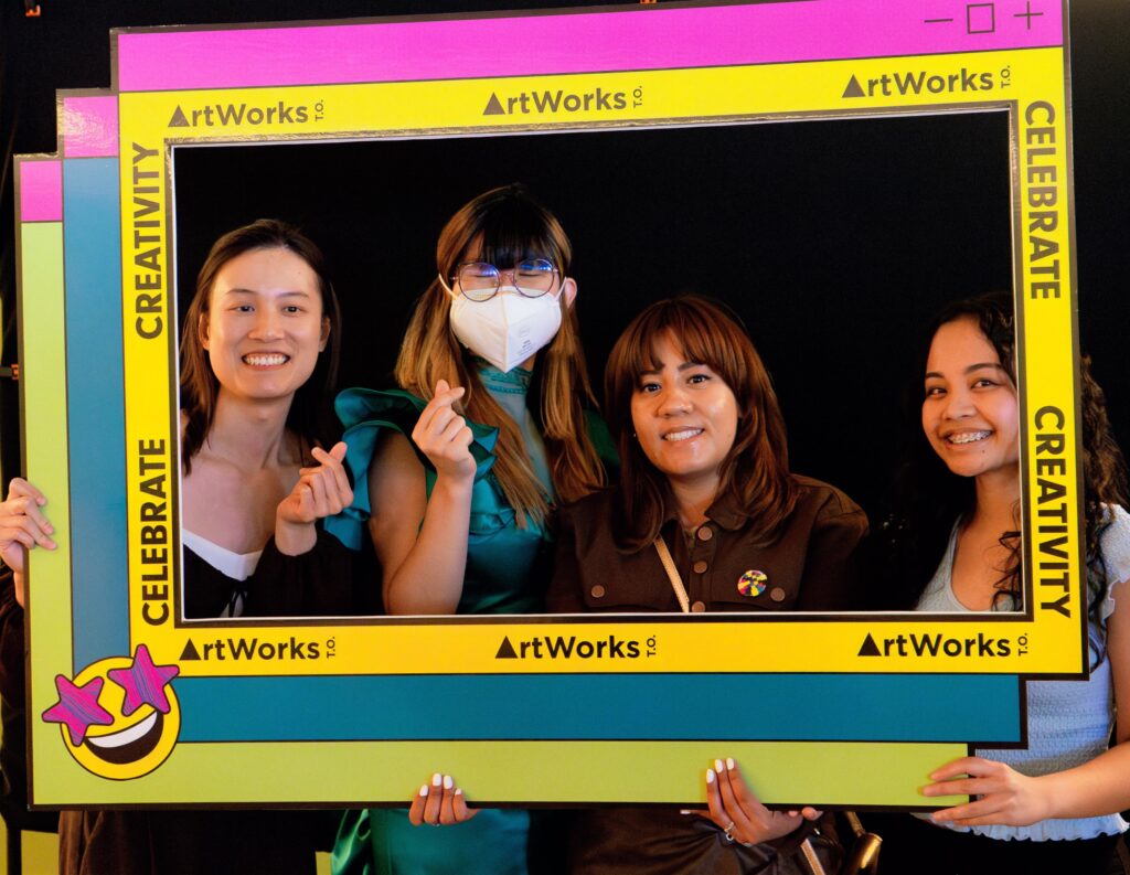 Four women media artists posing for a picture behind an ArtWorksTO cardboard frame which says Celebrate and Creativity