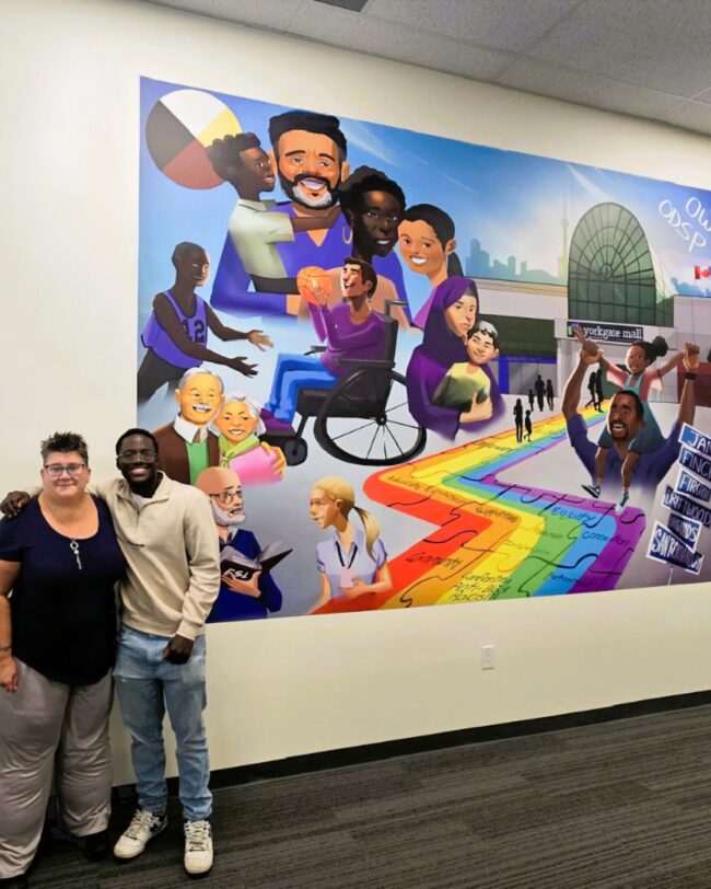 Artist Jerome is standing with host in front of his digital vinyl mural installed on a white wall