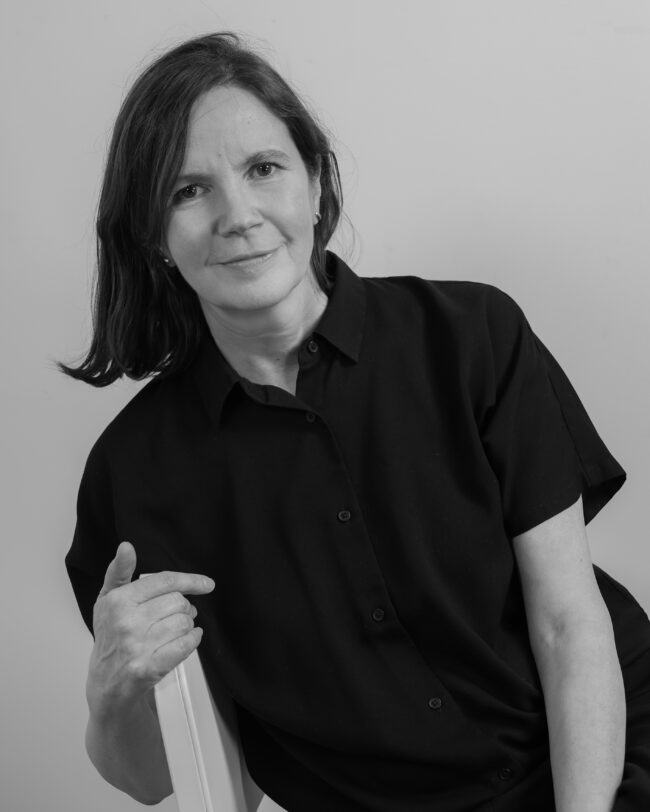 woman wearing a black short sleeved shirt looking at the viewer - sitting on a chair sideways - headshot photo