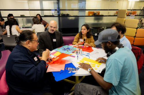 Participants in the ArtWorksTO interact at a Welcome Event, sitting at a table with art supplies.