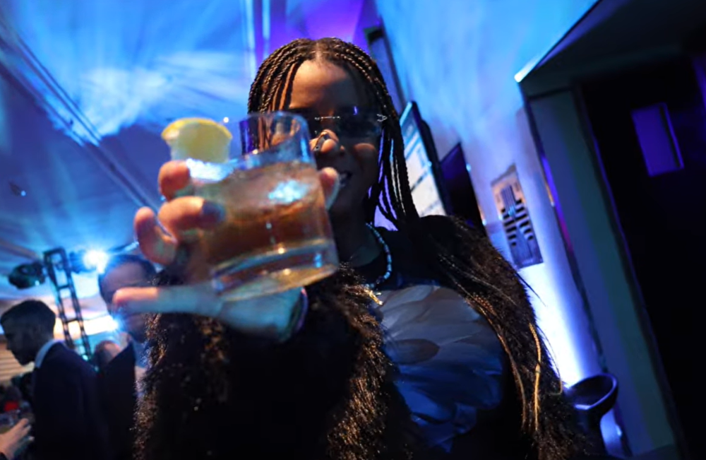 A person cheers the camera lens with a drink.