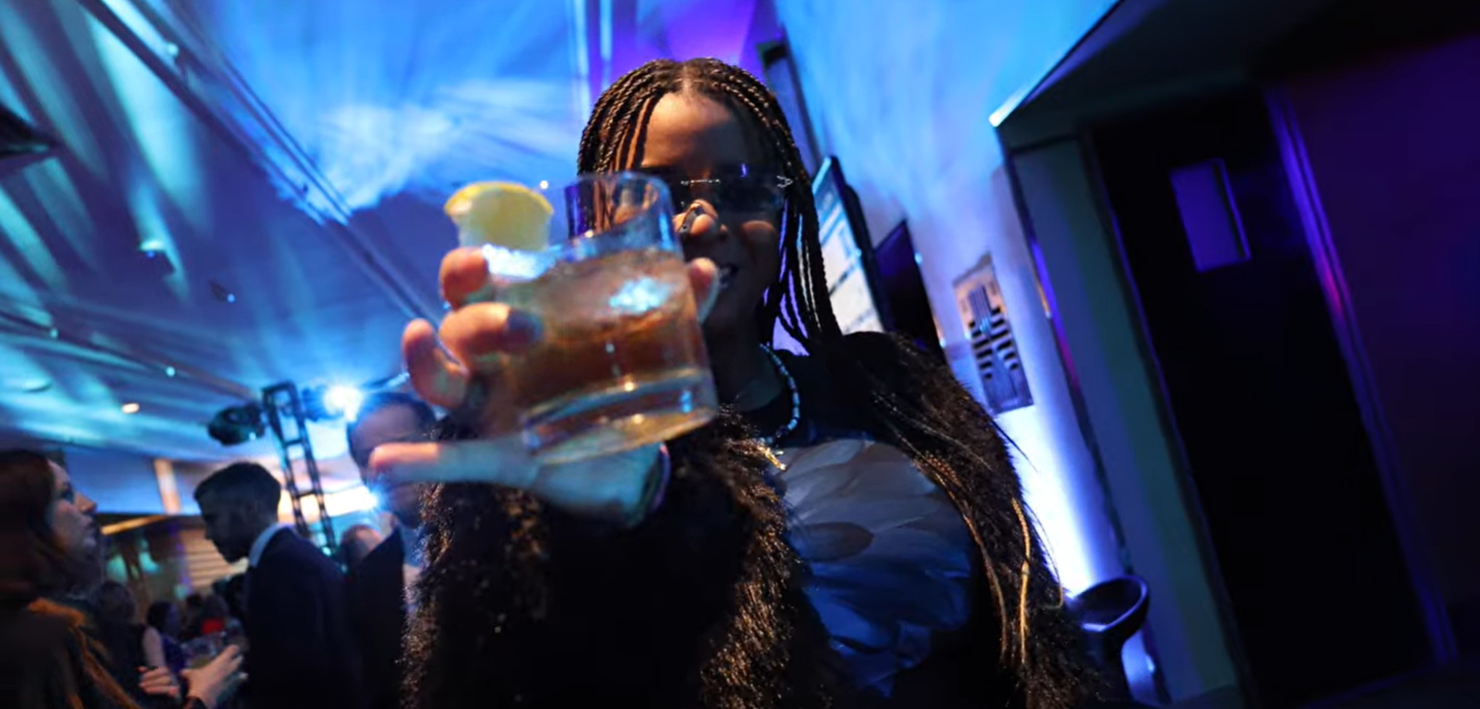 A person cheers the camera lens with a drink.