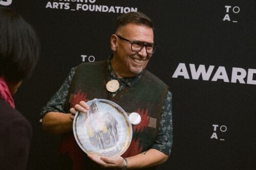 A man smiles holding an award plate.