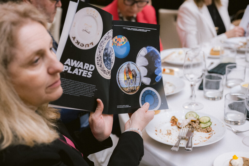 A person holds up a program book with images of past award plates.